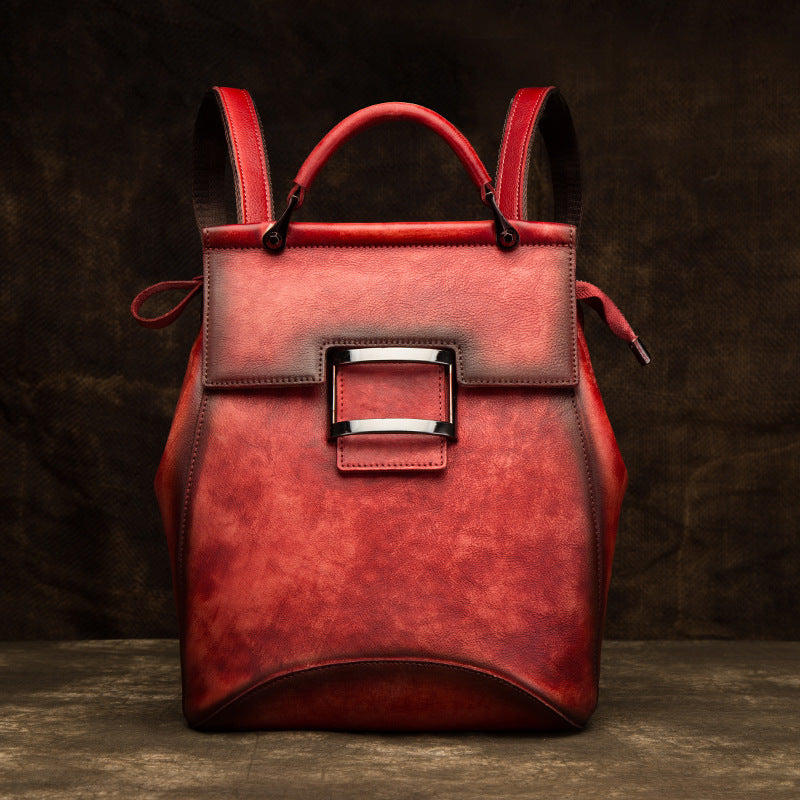 Front view of red top-grain cowhide backpack with handle and rectangular metal accent