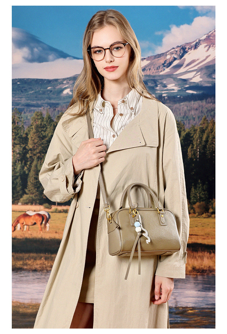 Model in a beige trench coat holding a taupe leather pillow bag in front