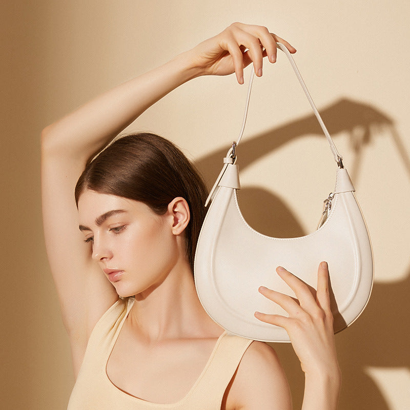 Model holding a cream white crescent shoulder bag by the top strap