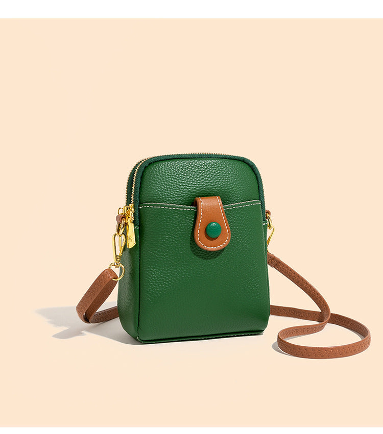 Green cowhide crossbody phone bag with pebbled leather and brown leather strap on beige background