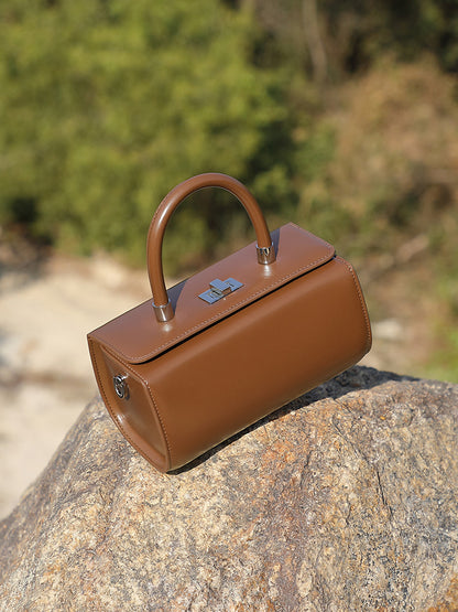 Coffee brown box handbag resting on a sunlit rock in an outdoor setting
