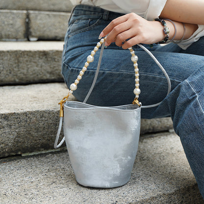 Silver gray mini bucket bag held by hand with pearl chain detail