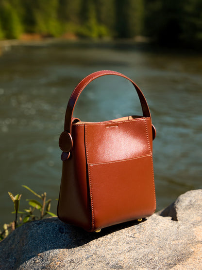 Brown leather bucket bag photographed on a rock by a river
