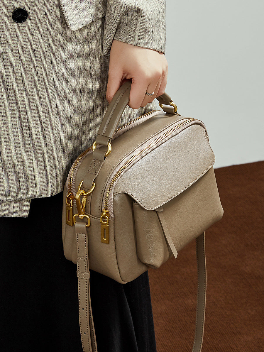 Top-grain cowhide Boston crossbody bag in taupe held by top handle, showing gold-tone hardware