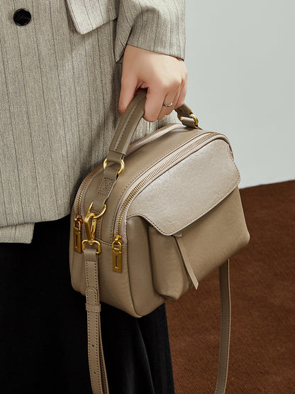 Top-grain cowhide Boston crossbody bag in taupe held by top handle, showing gold-tone hardware