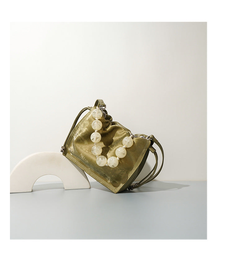 Lifestyle shot of champagne mini bucket bag displayed on a sculptural prop