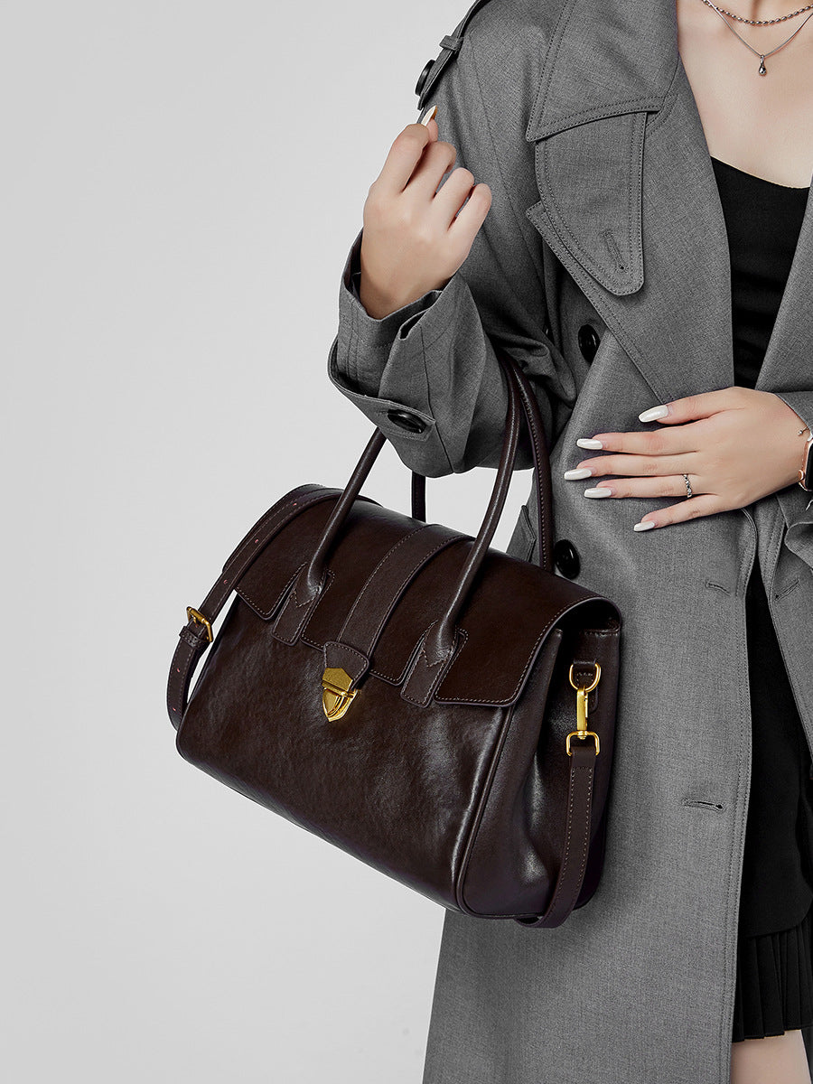 Dark brown leather satchel bag with gold-tone hardware on wooden table
