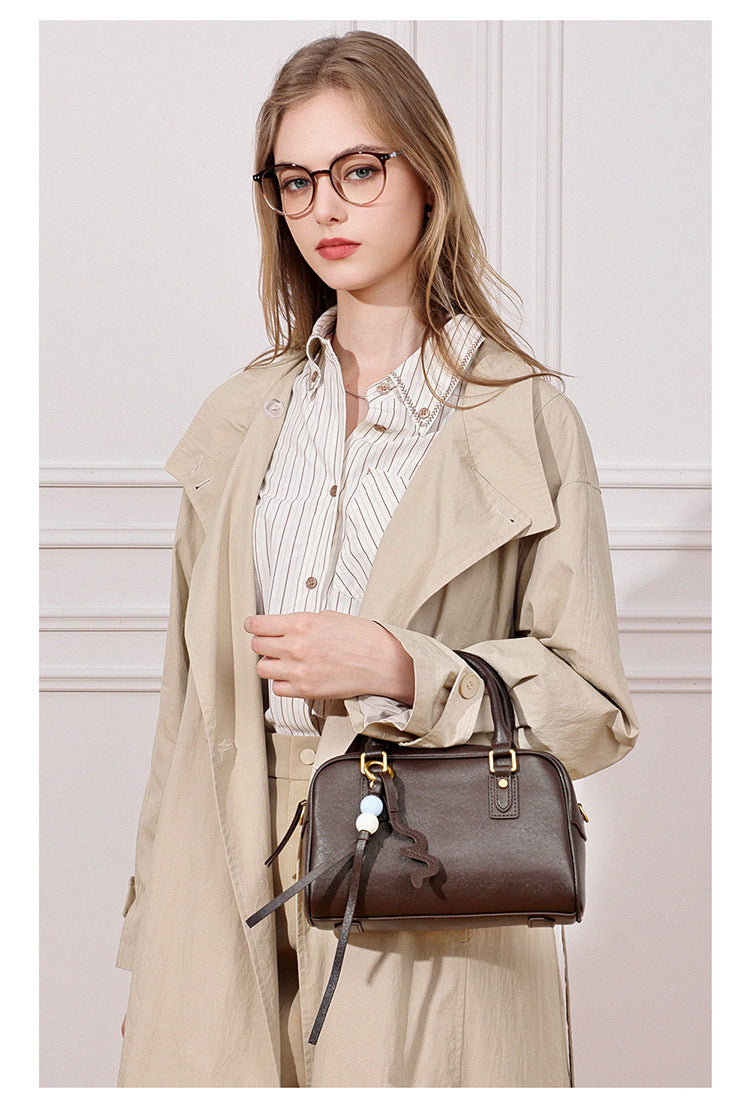 Model in a beige trench coat carrying a dark brown leather pillow bag by hand