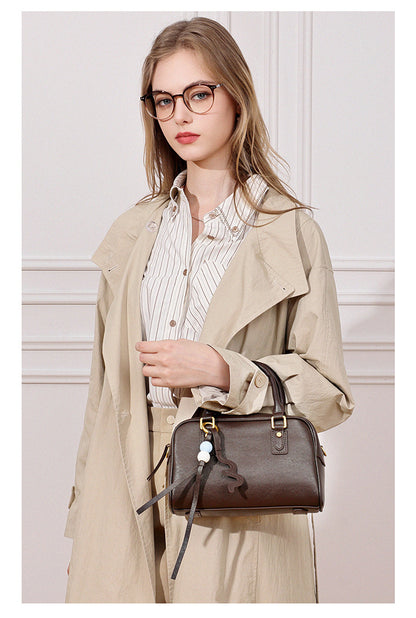 Model in a beige trench coat carrying a dark brown leather pillow bag by hand