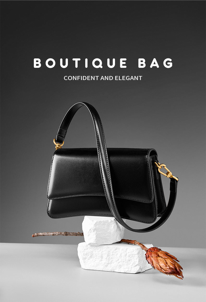 Boutique styled shot of black leather mini bag on stone pedestal with protea stem