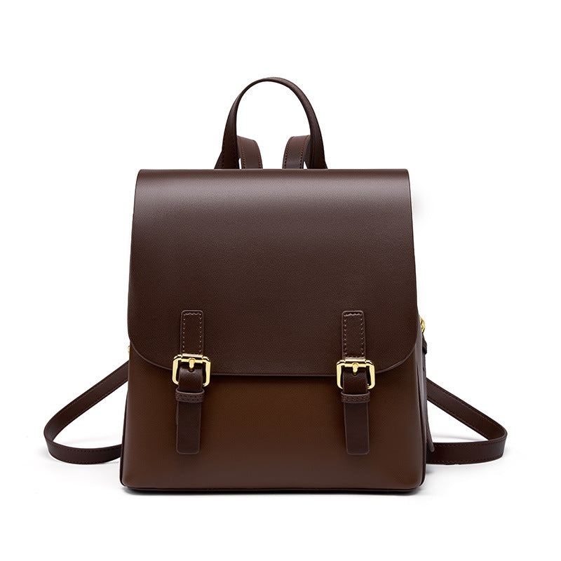 Dark brown cowhide leather backpack with two front magnetic strap closures and gold-tone buckles on a white background