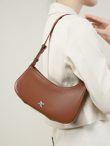Brown leather crescent bag worn on shoulder with white blazer