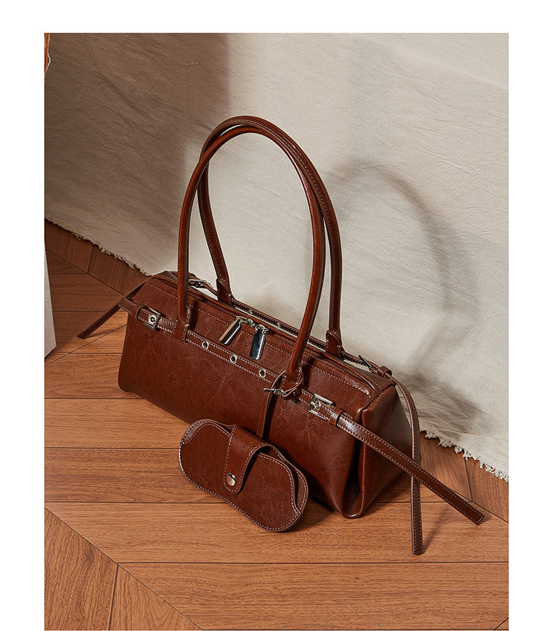 Brown leather barrel tote displayed on wooden floor with neutral fabric backdrop