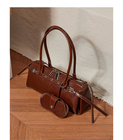 Brown leather barrel tote displayed on wooden floor with neutral fabric backdrop