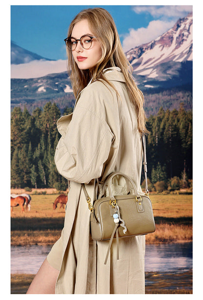 Model in a beige trench coat carrying a taupe leather pillow bag at her side