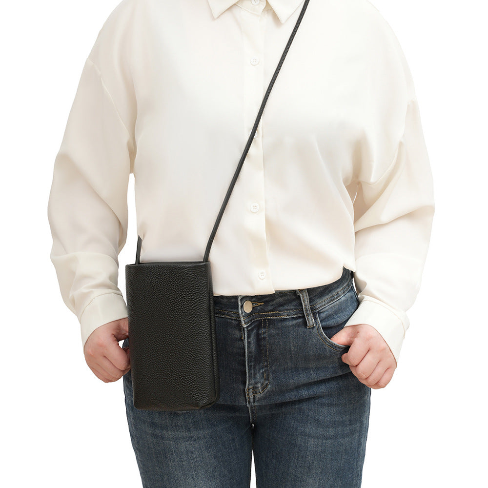 Black leather phone bag worn crossbody with cream blouse and denim jeans