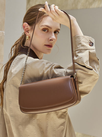 Brown cowhide baguette saddle bag held under the arm by a model in a beige jacket
