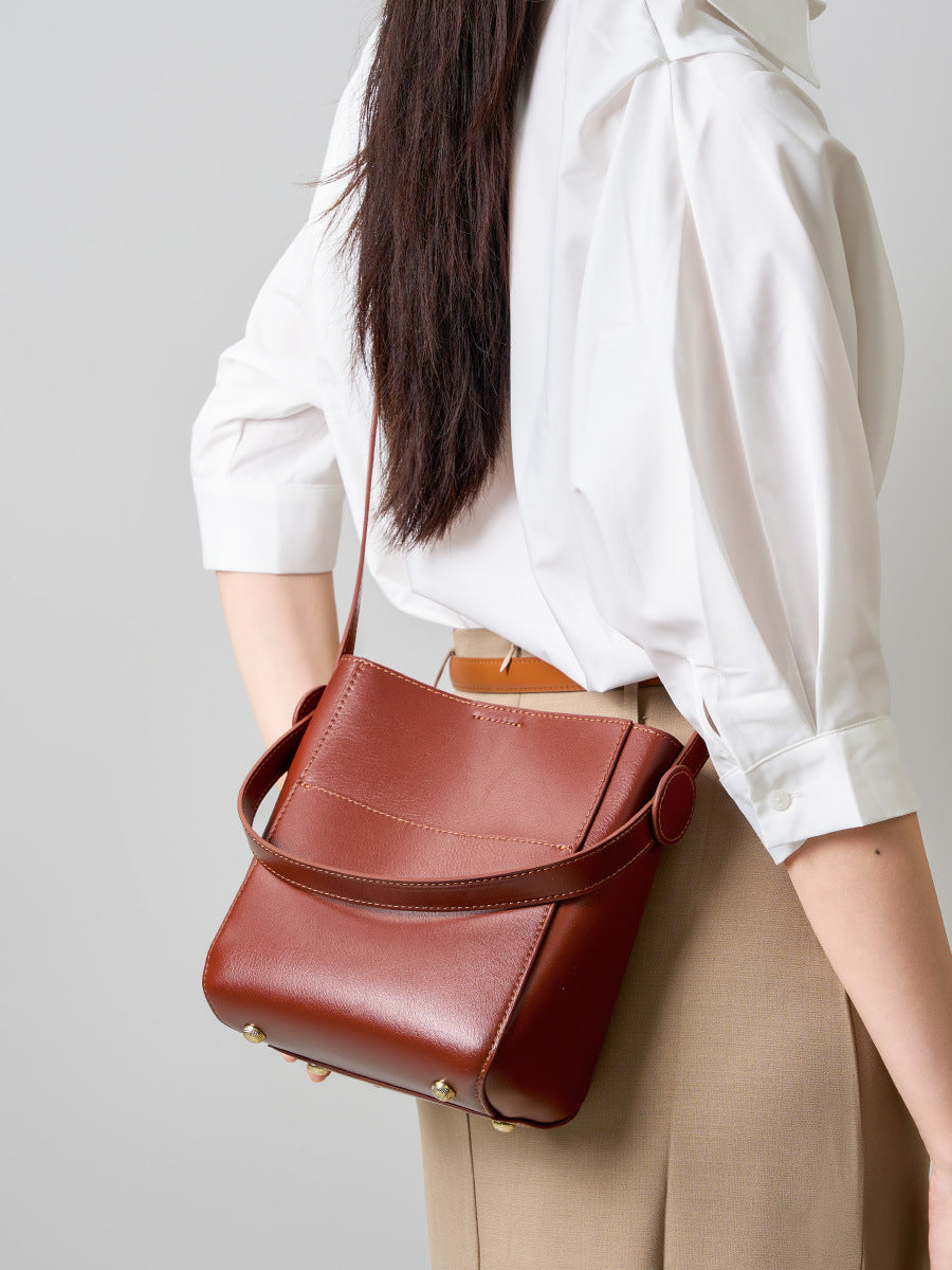 Brown cowhide bucket bag worn crossbody over a tan skirt