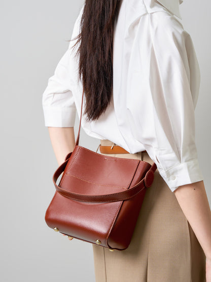 Brown cowhide bucket bag worn crossbody over a tan skirt