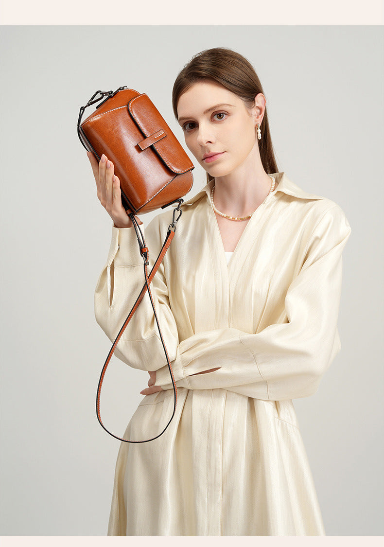 Model in cream blouse holding a caramel leather crossbody bag
