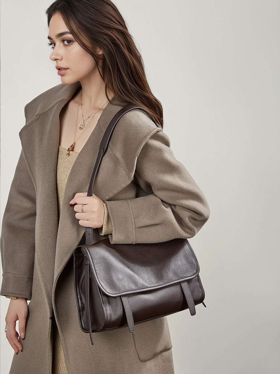 Model wearing dark brown leather messenger bag over the shoulder with a camel coat