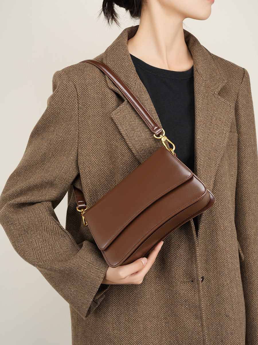 Close-up lifestyle shot of brown leather bag held under the arm with tailored coat