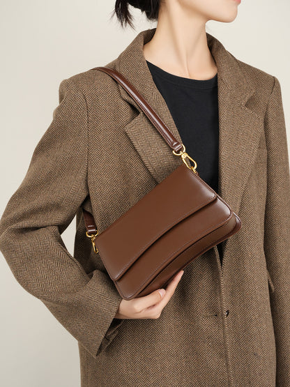 Close-up lifestyle shot of brown leather bag held under the arm with tailored coat