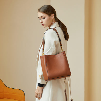 Model in cream coat carrying tan bucket tote bag on shoulder