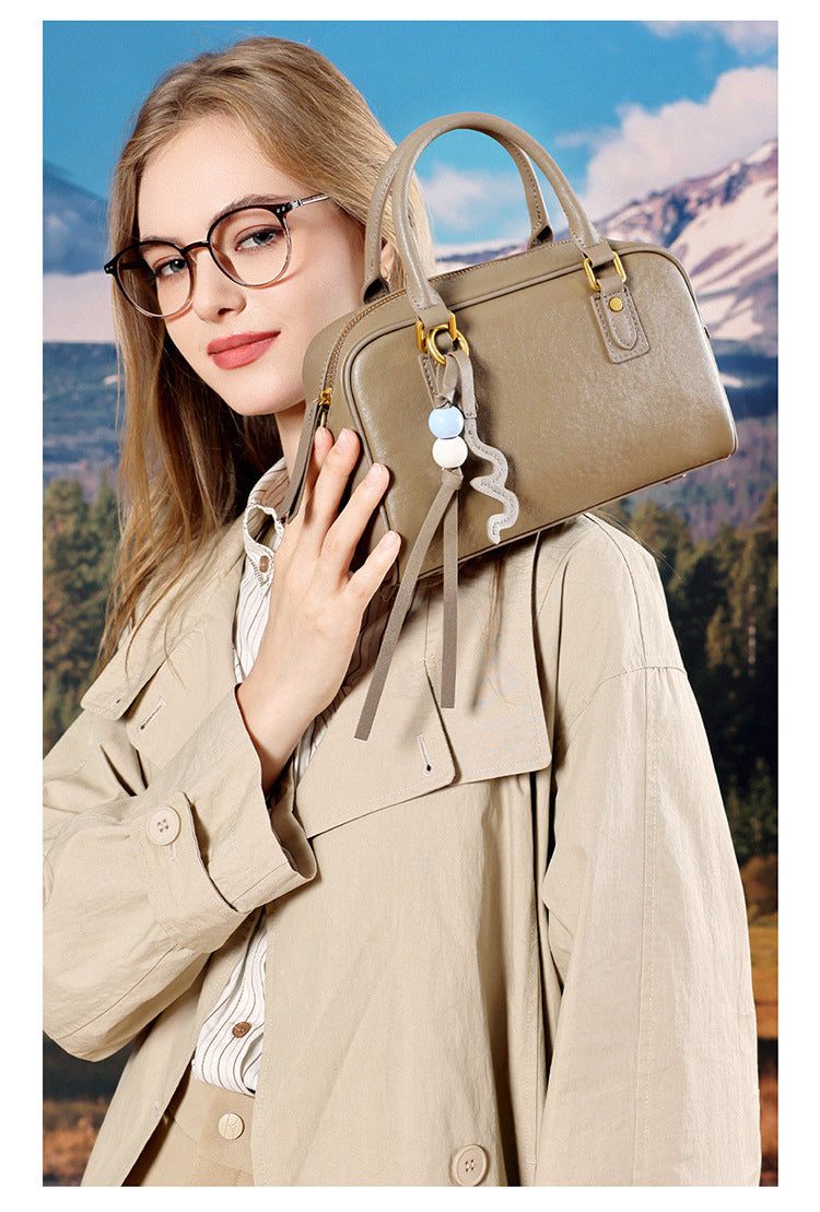 Model in a beige trench coat holding a taupe leather pillow bag against her shoulder