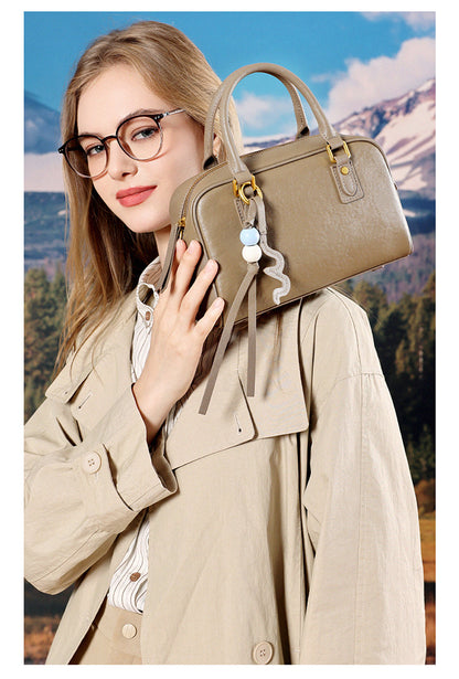Model in a beige trench coat holding a taupe leather pillow bag against her shoulder