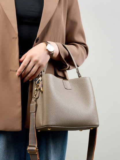 Brown leather bucket bag worn as a crossbody with a blazer