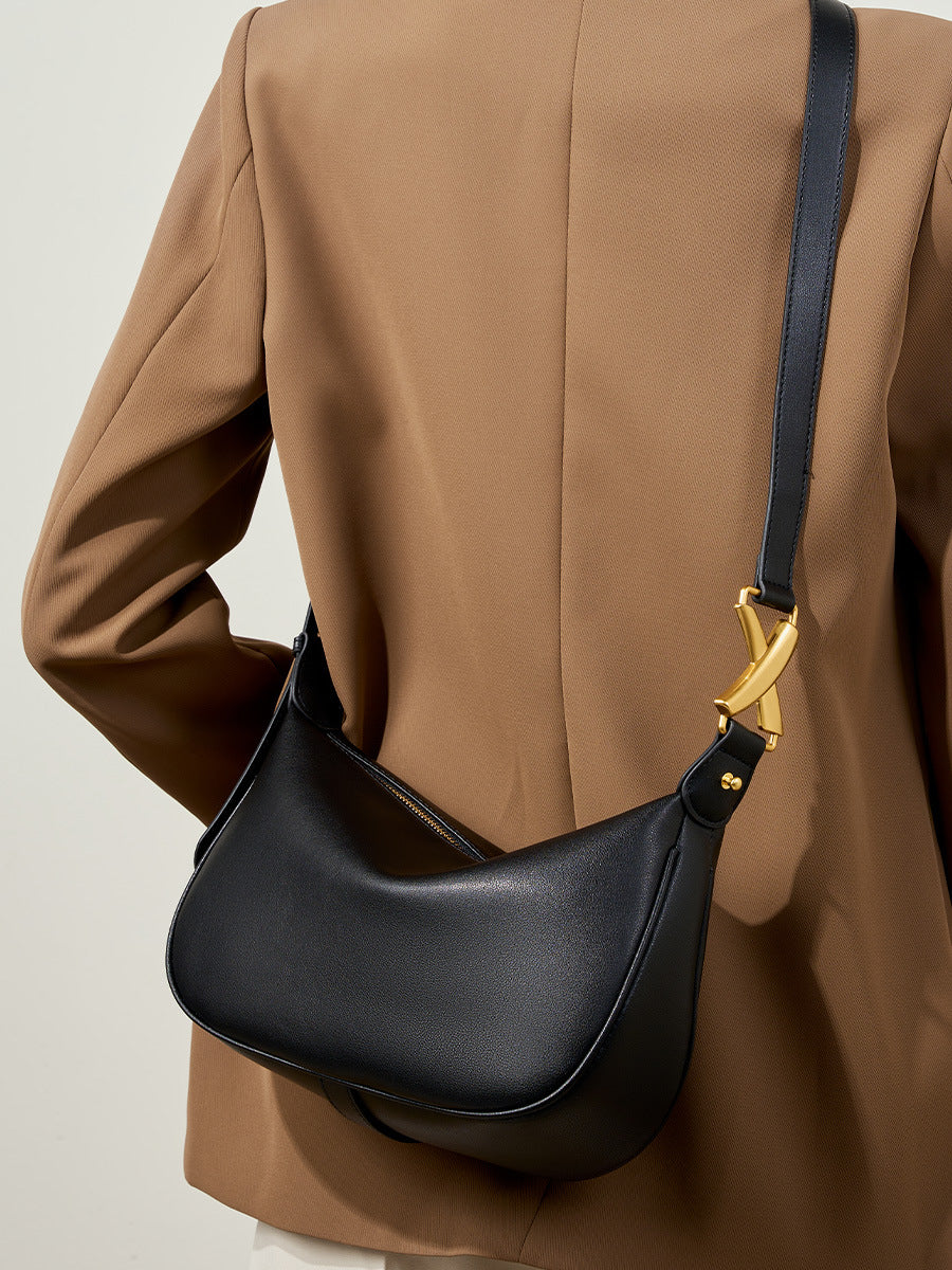 Black cowhide crescent underarm bag with gold-tone X buckle worn crossbody in lifestyle shot