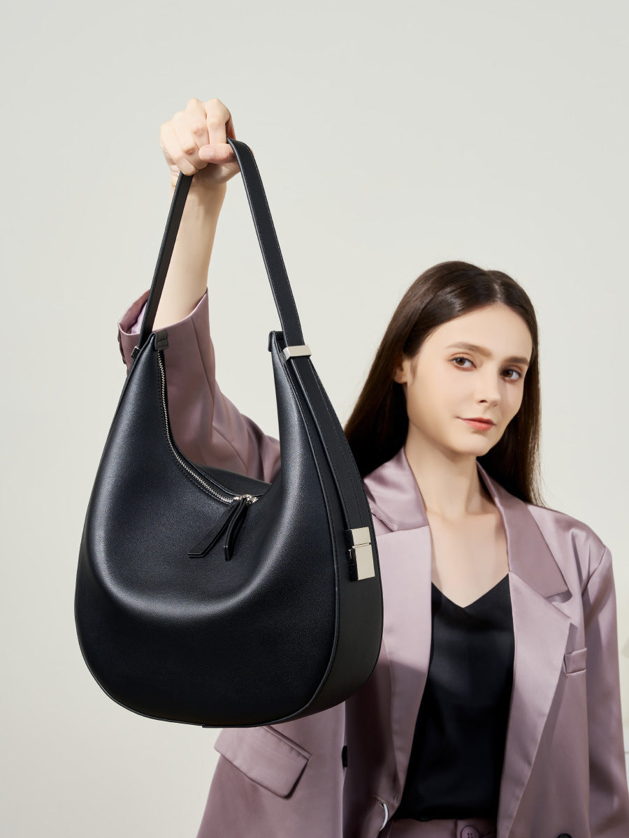 Model wearing a mauve blazer holding the black cowhide leather crescent hobo bag by the shoulder strap