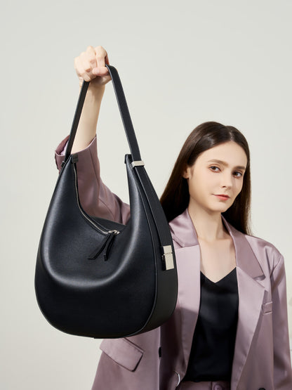 Model wearing a mauve blazer holding the black cowhide leather crescent hobo bag by the shoulder strap