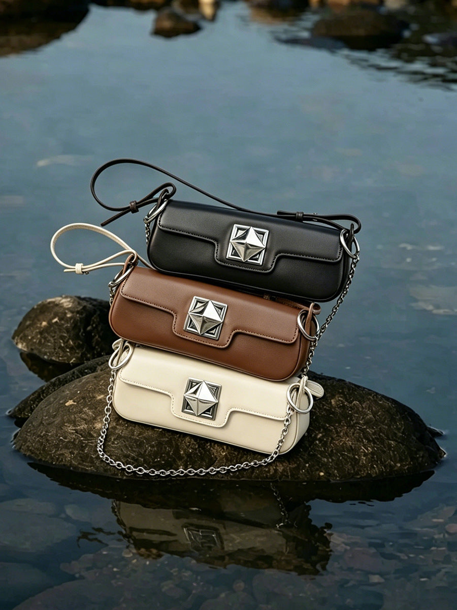 Stack of leather baguette bags in black, caramel, and off-white on a rock near water