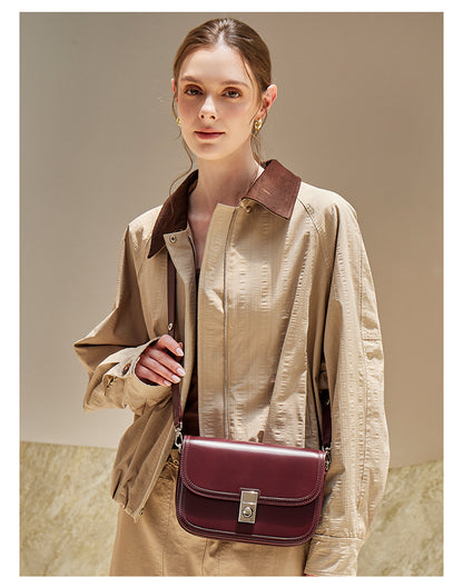 Wine red leather messenger bag worn crossbody in neutral outfit