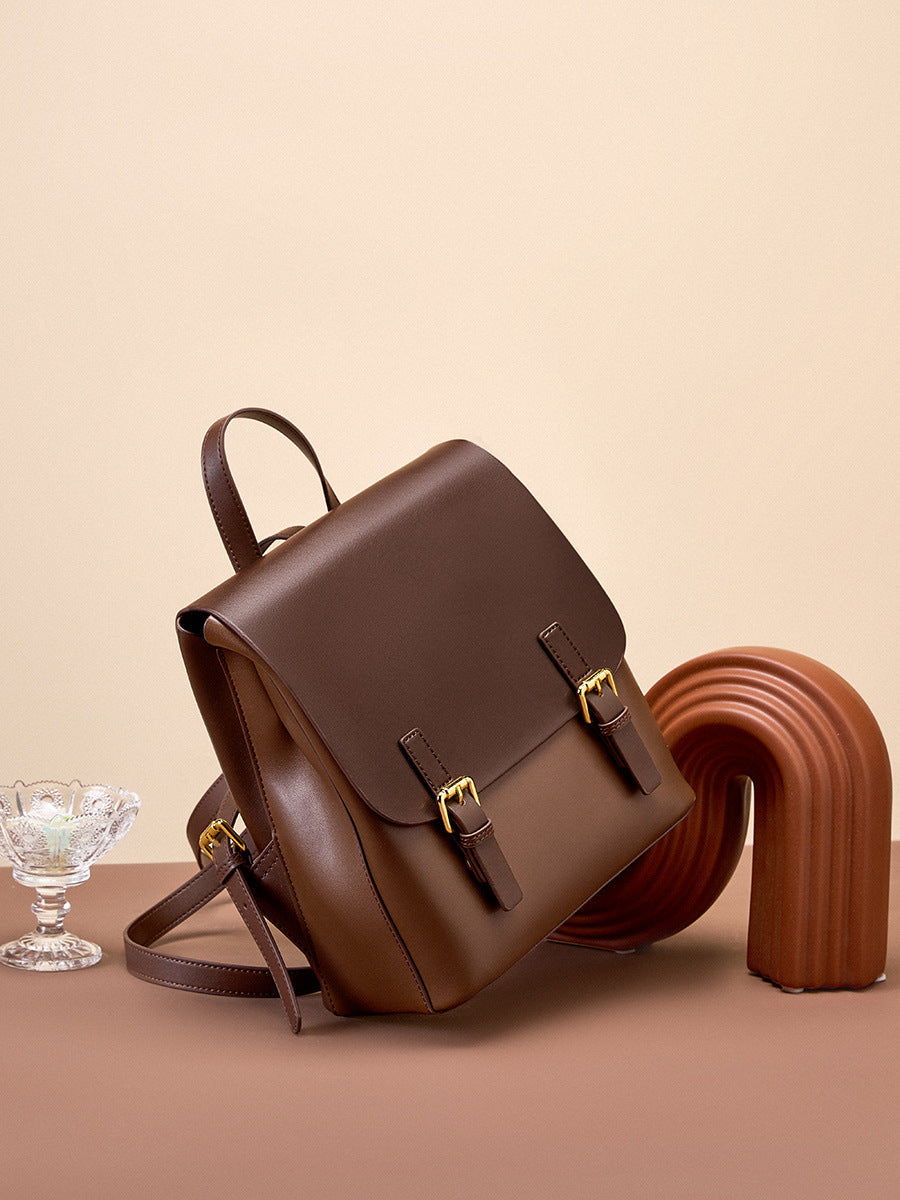 Dark brown leather backpack propped on a terracotta surface with a sculptural object and glass dish in the background