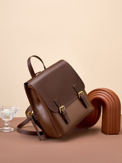 Dark brown leather backpack propped on a terracotta surface with a sculptural object and glass dish in the background