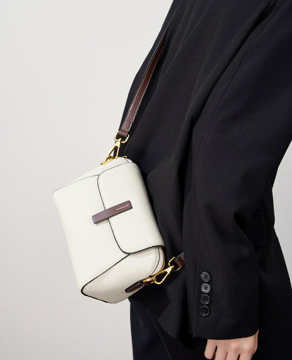Ivory shell crossbody bag worn crossbody with the strap fully visible against a black blazer