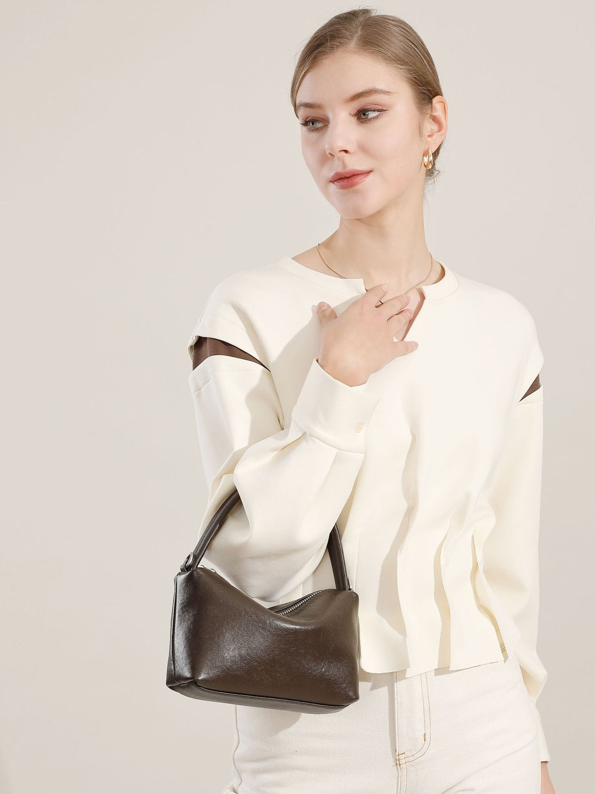 Brown leather pillow bag held by a model in a white top