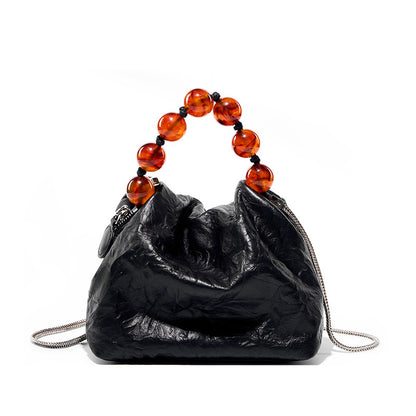 Black crinkle cowhide crossbody bag with amber bead handle on white background