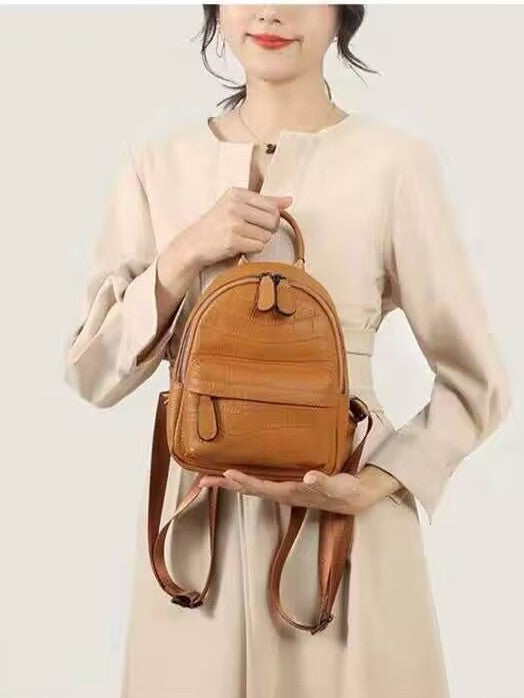 Front view of a tan crocodile-embossed backpack held by its top handle