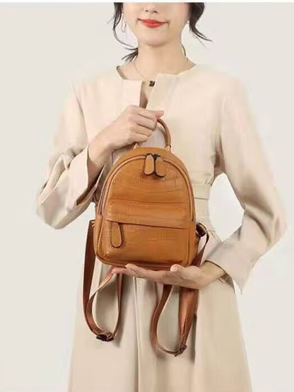 Front view of a tan crocodile-embossed backpack held by its top handle