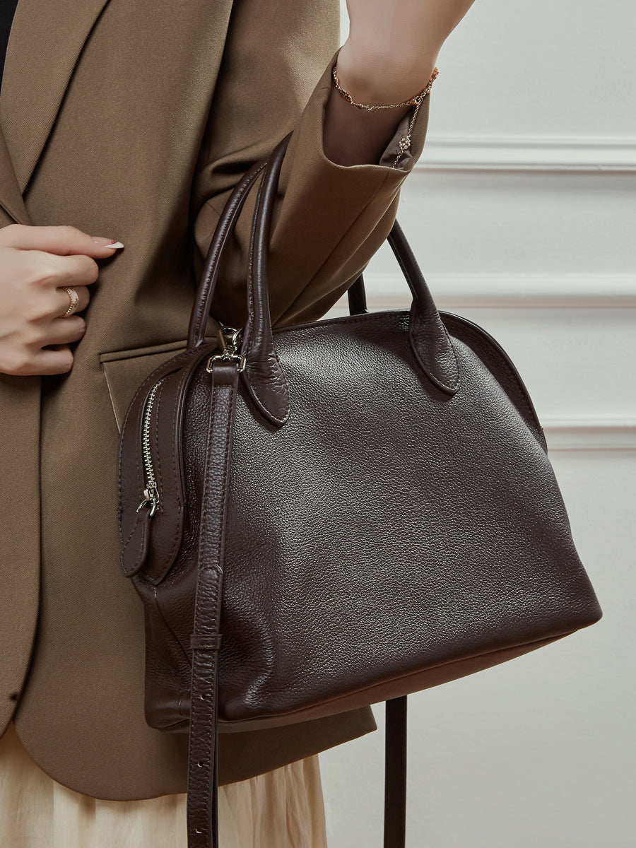 Model carrying a coffee brown leather bowling tote on the arm with a blazer