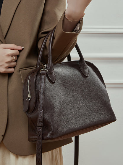 Model carrying a coffee brown leather bowling tote on the arm with a blazer