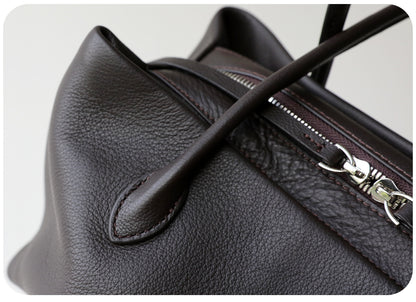 Close-up of tote handle stitching, leather grain, and zip hardware
