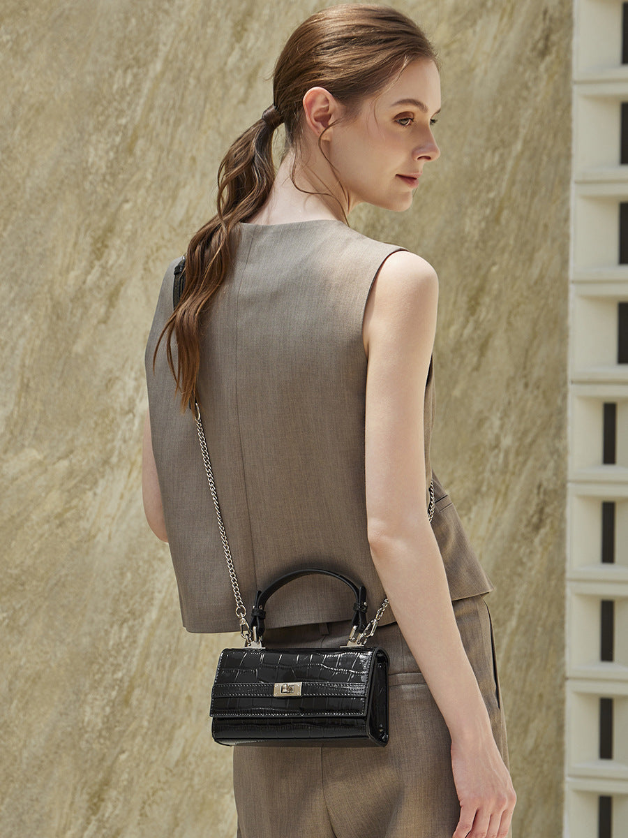 Model carrying black croco-embossed crossbody bag with chain strap in front three-quarter view