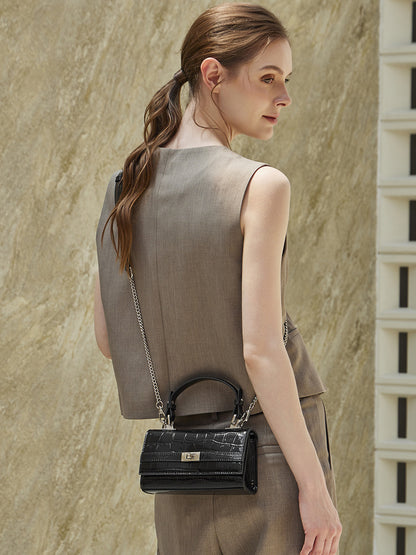Model carrying black croco-embossed crossbody bag with chain strap in front three-quarter view