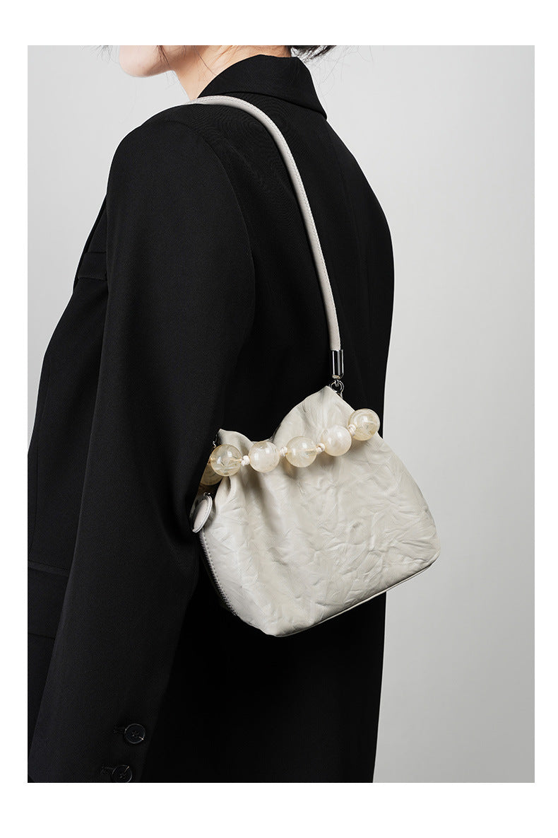 Off-white crinkle bag worn under the arm with chain strap and black coat
