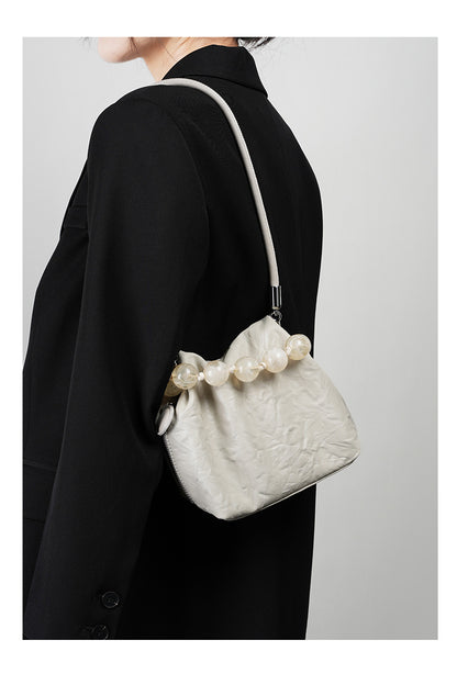 Off-white crinkle bag worn under the arm with chain strap and black coat